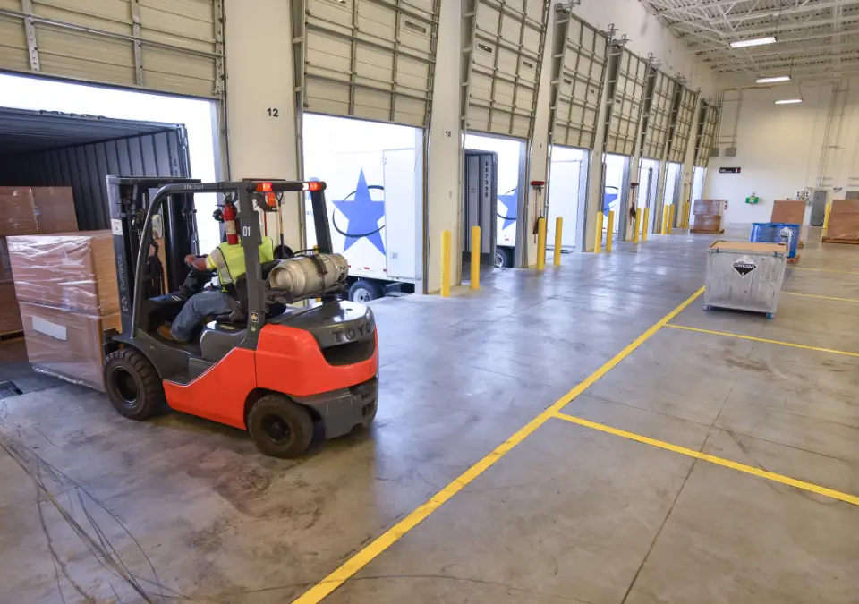 A forklift operator loads a large box into a truck.